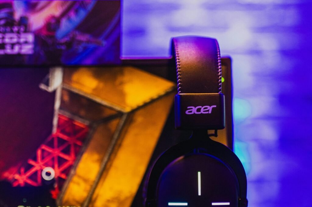 Close-up of a gaming setup featuring an Acer laptop and headset illuminated by colorful lights.